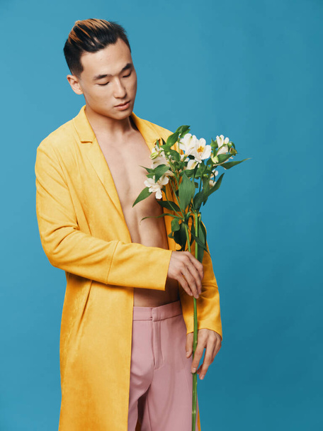 Ο τύπος με το κίτρινο παλτό. Ασιατική εμφάνιση. Μπουκέτο με λευκά λουλούδια μπλε φόντο - Φωτογραφία, εικόνα