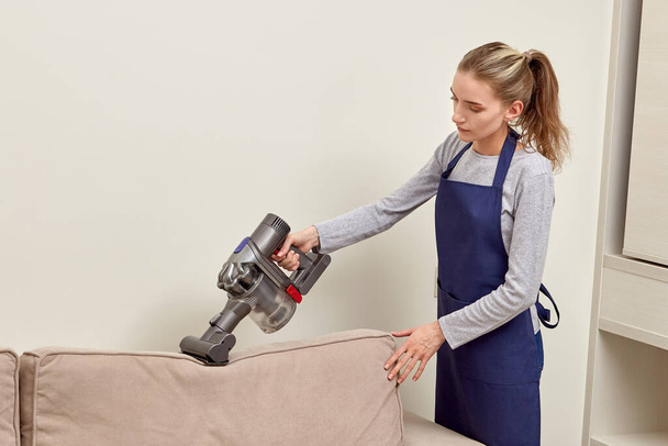 A woman vacuums the dust from the sofa cushion with a cleaning vacuum cleaner. - Foto, imagen