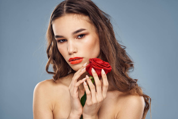 Portret kobiety z czerwoną różą w pobliżu twarzy na szarym tle i makijaż kręcone włosy - Zdjęcie, obraz