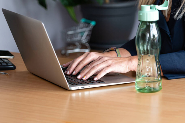 close-up of business woman hands working on laptop, in the foreground bottled water in the office on the desk - Photo, Image