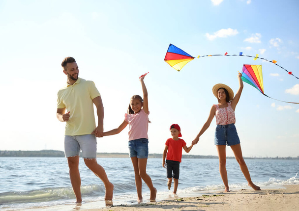 Happy parents and their children playing with kites on beach near sea. Spending time in nature - Foto, afbeelding