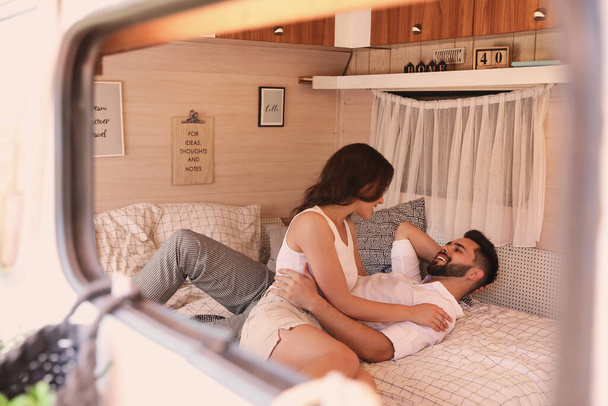 Happy young couple on bed in trailer, view from outside. Camping vacation - Foto, Imagem