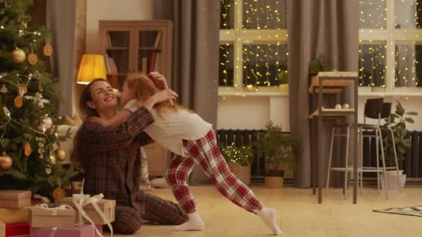Volledige shot van kleine zoete meisje met krullend rood haar lopen naar moeder zitten onder versierde kerstboom knuffelen en uitpakken van cadeautjes samen - Video