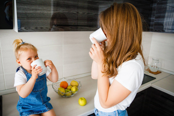 Mother is drinking tea in the kitchen with her little daughter. - Foto, imagen