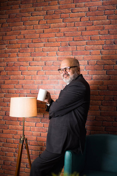 Portrait of Asian Indian businessman standing against brick wall with coffee mug - Photo, Image