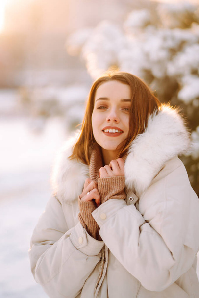 Portrait of young beautiful woman  in a snowy park. Cheerful lady in winter clothes posing with joy outside in the snow forest. Winter holiday, Christmas, New year. - Photo, image