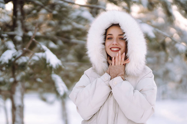 Portrait of young beautiful woman  in a snowy park. Cheerful lady in winter clothes posing with joy outside in the snow forest. Winter holiday, Christmas, New year. - Фото, зображення