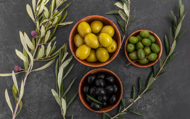 Olives marinées vertes et noires servies dans des bols avec des branches d'arbres frais. Alimentation méditerranéenne saine. - Photo, image