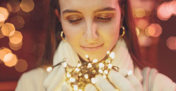 Happy young woman holding Christmas lights in her hands, holidays and celebrations concept - Foto, Bild