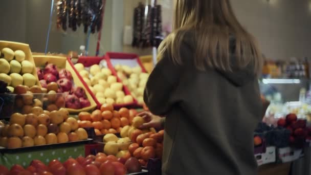 Vista posteriore della giovane donna sceglie prugne sugli scaffali dei negozi al mercato - Filmati, video
