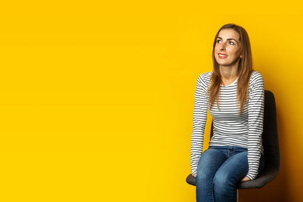 Une jeune femme souriante s'assoit sur une chaise sur fond jaune. Bannière. - Photo, image