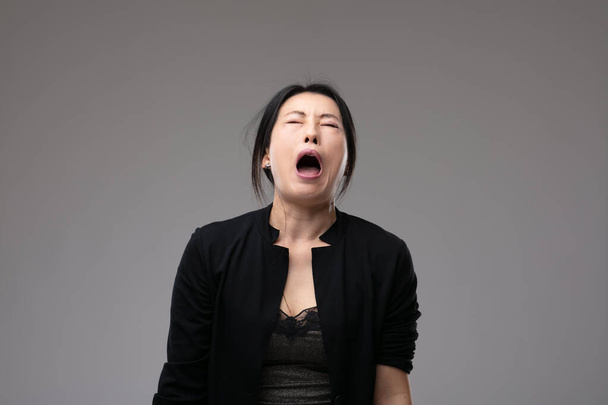 アジア系の女が苦悶の中で口を開けて悲しみの表情でコピースペースを持つ灰色のスタジオの背景 - 写真・画像