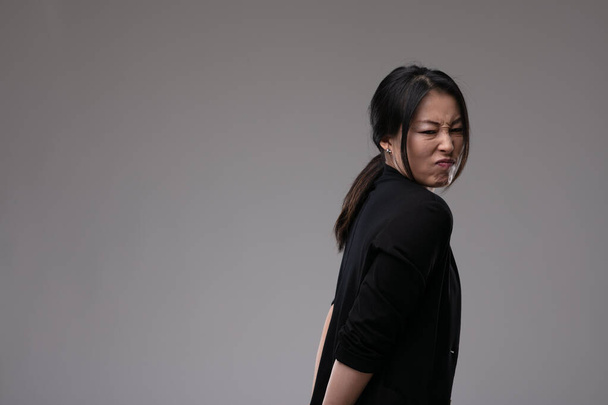 Verächtliche Asiatin, die ihren Ekel oder ihre Abneigung mit einer Fratze über einem grauen Studiohintergrund mit Kopierraum zeigt - Foto, Bild