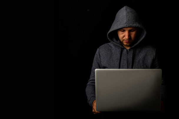 Mężczyzna w kapturze trzyma laptopa w rękach na ciemnym tle. Koncepcja cyberłotra, hakerze. Sztandar. - Zdjęcie, obraz