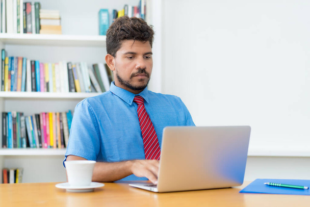 Latin american businessman listening and talking online at web conference at computer at office - Φωτογραφία, εικόνα