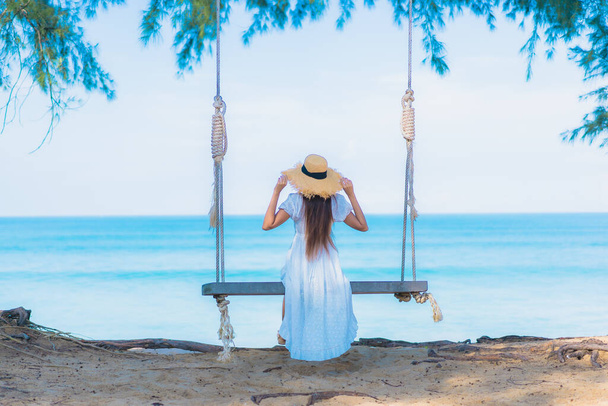 Ritratto bella giovane donna asiatica rilassarsi sorriso svago su swing intorno spiaggia mare oceano con blu cielo bianco nube - Foto, immagini