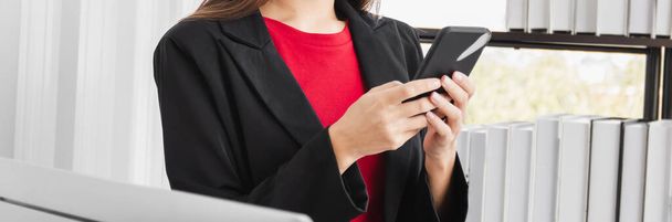 Mladá podnikatelka v černém obleku používá smartphone k chatování s obchodními partnery. - Fotografie, Obrázek