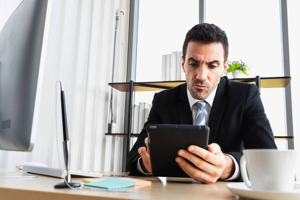 El jefe de negocios se está estresando sobre las relaciones comerciales, mientras que mirando a la tableta de la computadora. Un hombre de negocios haciendo hincapié en el trabajo en una tableta en la oficina. - Foto, imagen