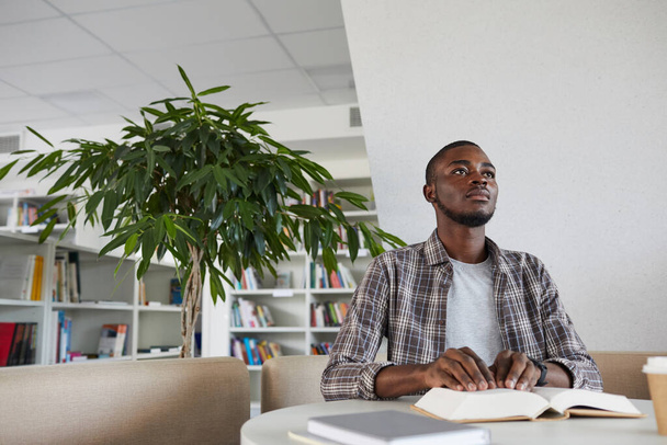 Малокутний погляд на сліпого афро-американського чоловіка, який читає книгу Брайля в шкільній бібліотеці, копіюю простору - Фото, зображення