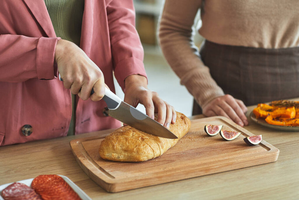 Akşam yemeği için yemek pişirirken taze ekmek kesen tanınmamış iki kadının fotoğrafını çek. - Fotoğraf, Görsel