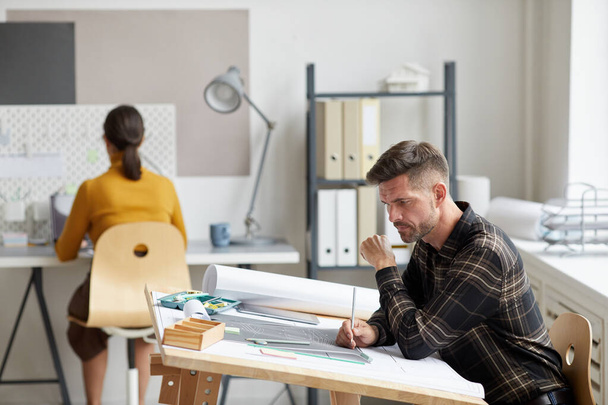 Boční pohled portrét zralého vousatého architekta pracujícího na plánech a plánech při sezení u kreslicího stolu v kanceláři, kopírovací prostor - Fotografie, Obrázek