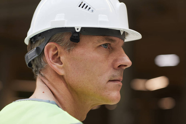 Вид сбоку портрет профессионального строителя в шлеме и смотрящего в сторону, копировальное пространство - Фото, изображение