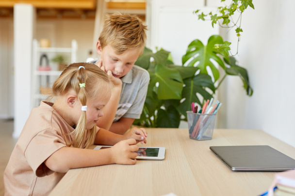 Retrato de vista lateral de una linda chica con síndrome de Down usando tableta digital con su hermano mayor mientras estudia en casa, espacio para copiar - Foto, imagen