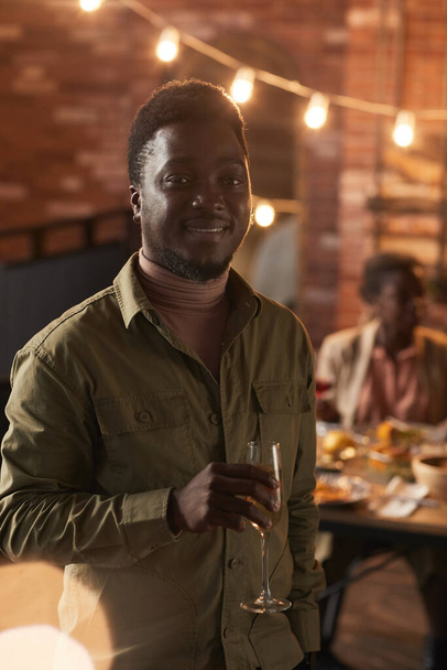 Вертикальная талия до портрета улыбающегося афроамериканца, держащего бокал шампанского и смотрящего в камеру, наслаждающегося вечеринкой на открытом воздухе - Фото, изображение