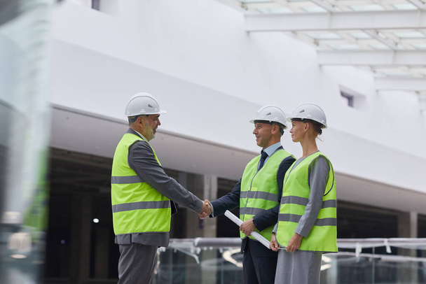 Side view portrait of smiling business people shaking hands after investment deal at construction site, copy space - Valokuva, kuva