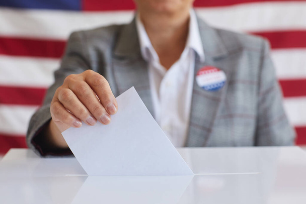 Primo piano della donna matura che mette il bollettino di voto nelle urne mentre si alza contro la bandiera americana il giorno delle elezioni, copia lo spazio - Foto, immagini