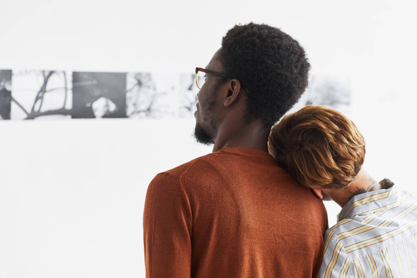 Graphic portrait of mixed-race couple embracing while looking at paintings at modern art gallery exhibition, copy space - Foto, afbeelding