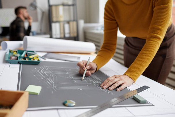 Обрезанный снимок неузнаваемой женщины-архитектора, рисующей чертежи и планы во время работы за столом в офисе, копирующее пространство - Фото, изображение