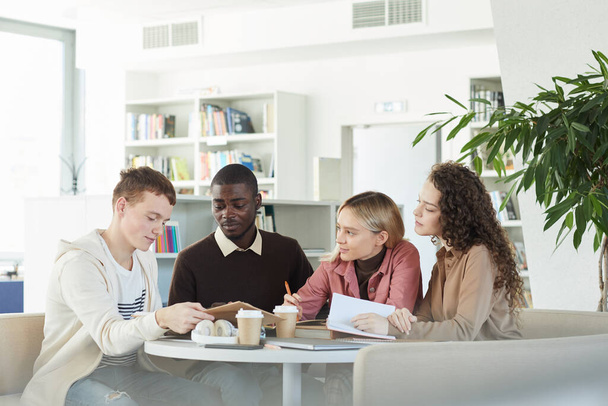 Multiethnische Gruppe junger Leute, die zusammen lernen, während sie am Tisch in der Universitätsbibliothek sitzen und an einem Gruppenprojekt arbeiten, Kopierraum - Foto, Bild