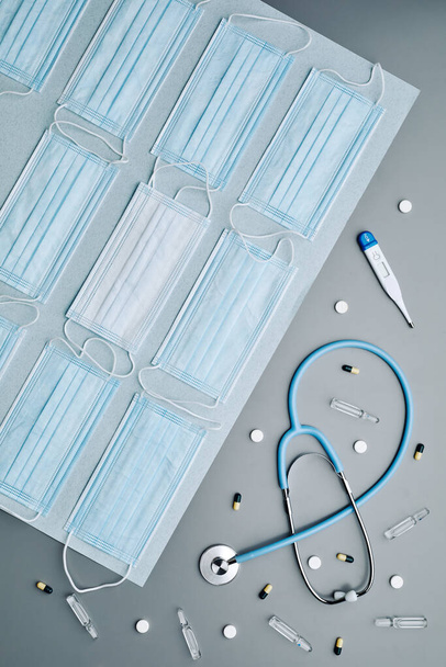 Top down graphic composition of medical masks with stethoscope and thermometer laid out over grey background, copy space - Photo, Image