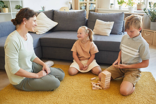 Retrato de larga duración de la familia amorosa con necesidades especiales niño jugando juegos de mesa mientras está sentado en el suelo en casa, espacio de copia - Foto, Imagen