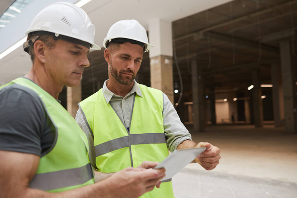 Портрет двох професійних будівельників, що використовують цифровий планшет, стоячи на будівельному майданчику, копіювати простір
 - Фото, зображення