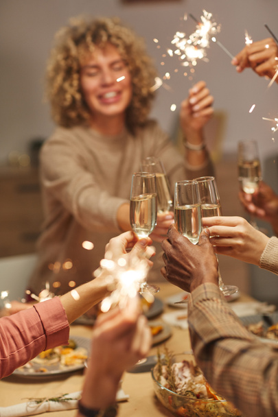Primer plano vertical de personas brindando con copas de champán mientras disfrutan de la cena con amigos y familiares y celebrando chispas - Foto, Imagen