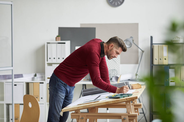 Widok z boku portret brodatego architekta rysującego plany opierając się na biurku w miejscu pracy, przestrzeń do kopiowania - Zdjęcie, obraz