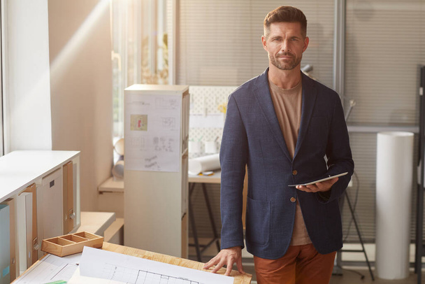 Warm toned portrait of handsome mature man looking at camera while standing by desk in office, copy space - Photo, Image