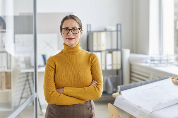 Kendine güvenen bir kadın mimarın belden yukarı portresi kameraya bakıyor ve kolları ofiste çapraz durarak gülümsüyor, boşluğu kopyalıyor. - Fotoğraf, Görsel