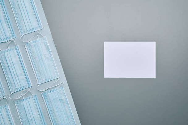 Composizione grafica dall'alto verso il basso di maschere mediche con carta bianca vuota disposta su sfondo grigio, spazio di copia - Foto, immagini