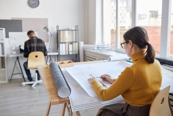 Πλάτη άποψη πορτρέτο της γυναίκας αρχιτέκτονα σχέδιο, ενώ κάθεται από το γραφείο στο γραφείο, αντίγραφο χώρο - Φωτογραφία, εικόνα