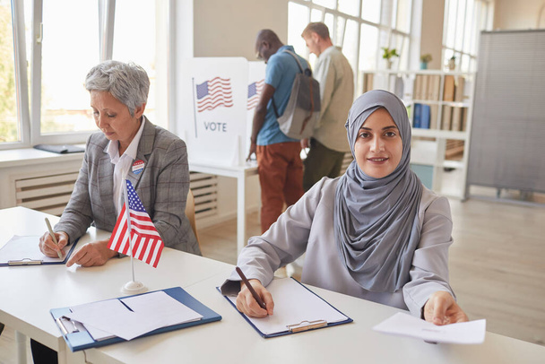 Portrait d'une Arabe souriante remettant des papiers à un électeur alors qu'elle travaillait au bureau de vote, photocopiant de l'espace - Photo, image
