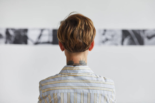 Vista posterior gráfica retrato de mujer joven tatuada mirando pinturas en la exposición de arte contemporáneo, espacio de copia - Foto, imagen