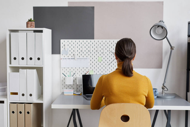 Retrato de vista trasera de una mujer adulta que usa un portátil mientras trabaja en el escritorio en casa o en la oficina, espacio para copiar - Foto, Imagen