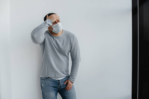 A young man stands on a gray background wearing a mask during a quarantine with free space. Quarantine in the mask - Fotoğraf, Görsel