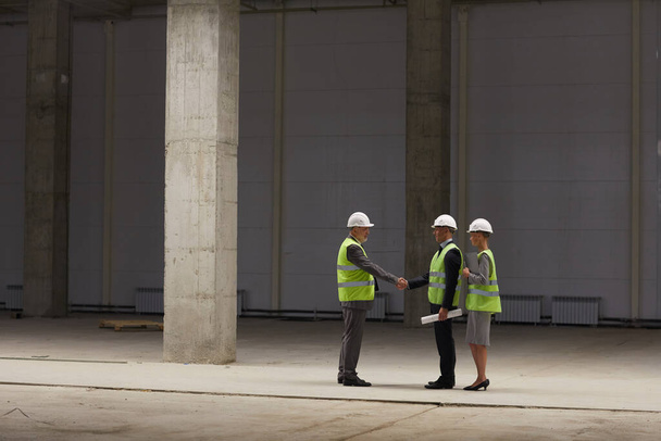 Portrait grand angle de gens d'affaires serrant la main tout en discutant affaire d'investissement sur le chantier de construction à l'intérieur, espace de copie - Photo, image