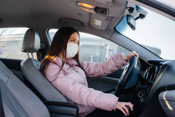 A young girl sits behind the wheel in the car in the mask during the global pandemic and coronavirus. Quarantine - Valokuva, kuva