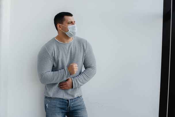 A young man stands on a gray background wearing a mask during a quarantine with free space. Quarantine in the mask - 写真・画像