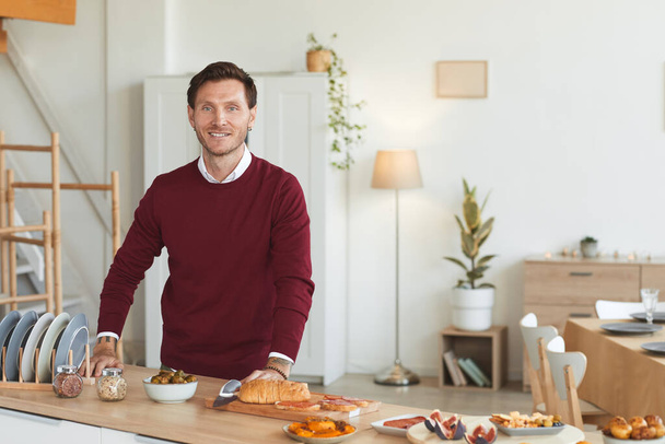 Талия портрет современного взрослого мужчины, смотрящего в камеру и улыбающегося во время приготовления пищи для званого ужина в помещении, копировальное пространство - Фото, изображение